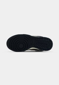 Semelle en caoutchouc noir d'une chaussure Nike présentant des motifs de bande de roulement circulaires et en grille avec le logo Nike visible au centre.