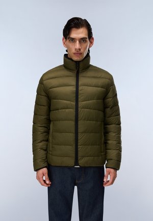 Homme faisant face à l'avant portant une doudoune vert olive zippée et un jean bleu foncé sur un fond clair uni.