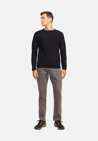 Camisa de manga larga azul marino oscuro con cuello redondo, puños acanalados, combinada con jeans grises y zapatillas negras. Diseño minimalista con un ajuste relajado.