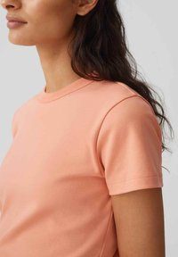 T-shirt a maniche corte, con collo a giro in colore corallo chiaro. Tessuto di cotone liscio con texture uniforme e cuciture pulite lungo i bordi.