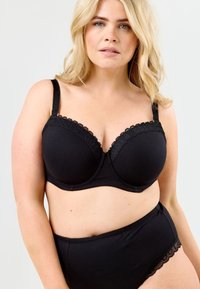 Svart behå med byglar och vågigt spetskant, justerbara axelband och matchande högmidjad trosor, båda tillverkade av mjukt tyg.