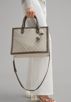 Sac fourre-tout beige avec un design à motifs, accents marron, poignées doubles, bandoulière amovible et détail en pompon. Matériau texturé.