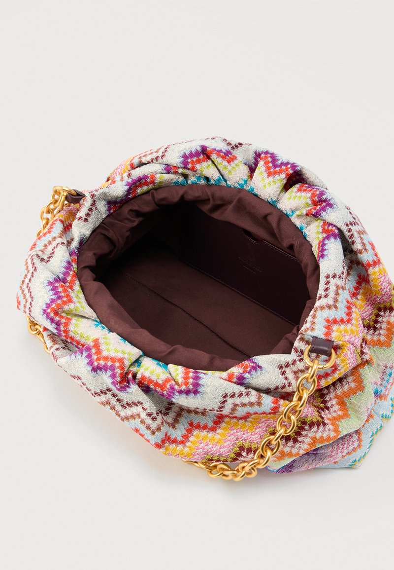 Kleurrijke tas van stof met zigzagpatroon, bruine binnenkant, open bovenkant en gouden kettingriem op een lichte achtergrond.