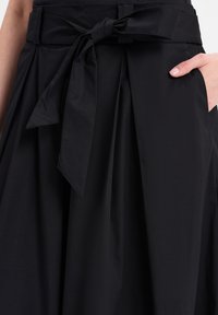 Zwarte rok met een ceintuur in de taille, met plooien, een gladde textuur en een zijzak, ontworpen met een stoffen strikaccent op de ceintuur.