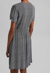 Schwarz-weißes Blumenmusterkleid mit kurzen Puffärmeln, einer gerafften Taille und einem fließenden Rock. Der Stoff hat ein weiches, strukturiertes Aussehen.