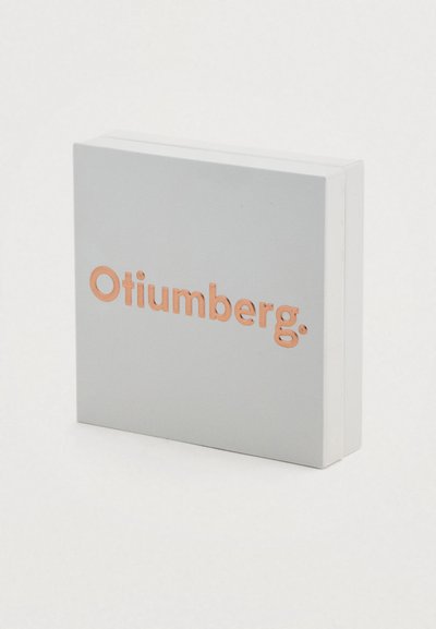 Τετράγωνο κουτί σε ματ ανοιχτό γκρι με ανάγλυφο, χαλκοχρώμιο λογότυπο "Otiumberg." Ομαλή υφή και καθαρός σχεδιασμός με στρογγυλεμένες άκρες.