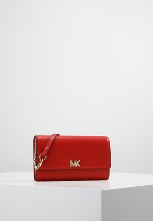 Pochette en cuir rouge Michael Kors avec bandoulière chaîne dorée et logo MK sur le devant, exposée sur un socle blanc.