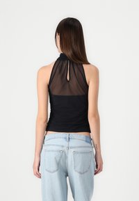 Schwarzes Neckholdertop mit transparentem Rücken, das über ein Schlüssellochdetail und Raffung an den Seiten verfügt, kombiniert mit hellblauen High-Waist-Jeans.
