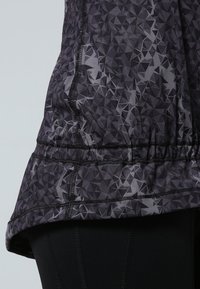 Svart och grå mönstrad träningsöverdel med geometrisk design, med ett gathered nederkant och svart sömdetalj.