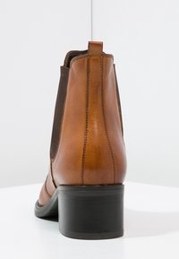 Stivale alla caviglia in pelle marrone con pannelli laterali elasticizzati, punta rotonda e tacco a blocco nero. Texture liscia con dettagli di cucitura sottili.