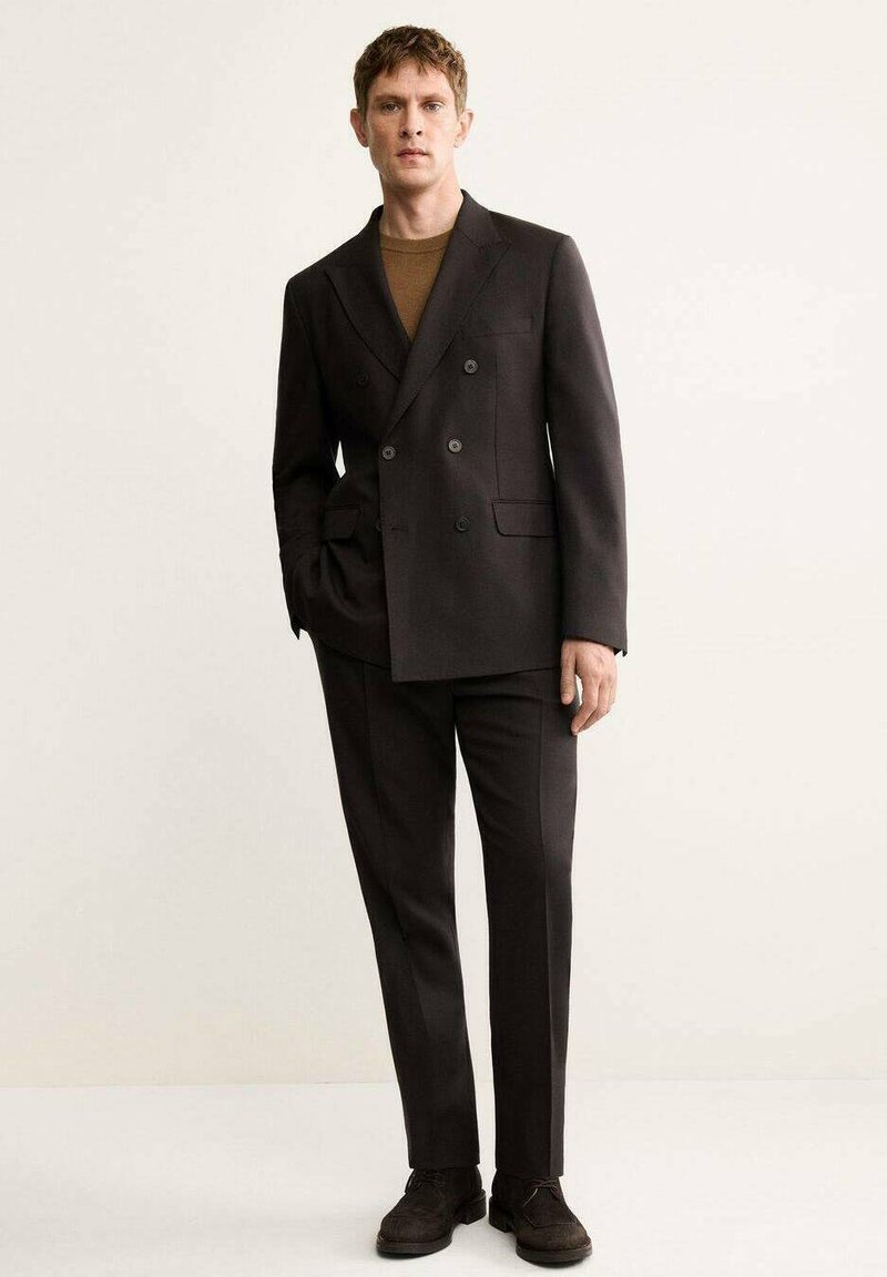 Dark brown double-breasted blazer paired with matching trousers. Textured fabric, slim fit, and black button accents. Brown suede shoes.