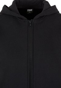 Crna zip-up dukserica s mekanim materijalom, visokim vratom i kapuljačom. Ima središnji zatvarač i bez vidljivih logotipa ili uzoraka.