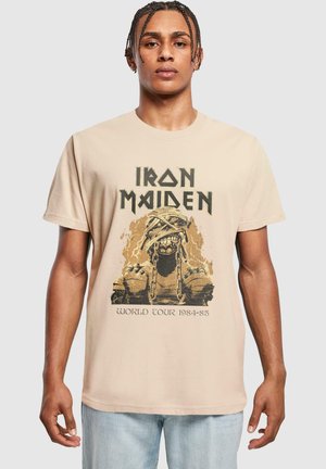 Beige bomulds T-shirt med et grafisk design af en kædret figur og tekst, der siger "Iron Maiden World Tour 1984-85".