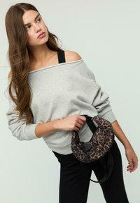 Felpa grigia off-the-shoulder, pantaloni neri, che tiene una borsa a forma curva con motivo leopardato marrone e nero e una tracolla.