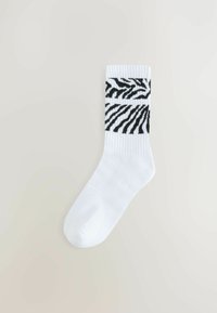 Bijela pamučna čarapa s crnim uzorkom zebra prugica na vrhu, s rebrastom teksturom oko manžetne i glatkim dijelom na prstima.