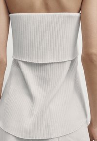 Top a tubo bianco a costine con un design a strati. Presenta una texture sottile e un orlo curvo, offrendo una silhouette aderente.