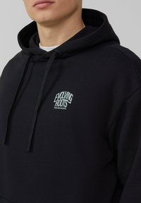 Zwarte hoodie gemaakt van katoen met een kangoeroe-pocket, met een klein lichtblauw logo op de borst dat "Evolving Roots" leest.