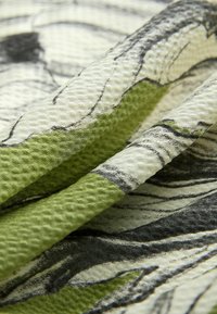 Tissu présentant une surface texturée avec un motif dans des tons de vert et de gris. Le design comprend des motifs abstraits et des blocs de couleur variés.