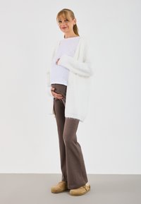 White fluffy cardigan over a white top, paired with ribbed brown flared pants and tan clogs. Simple, soft textures and neutral colors.