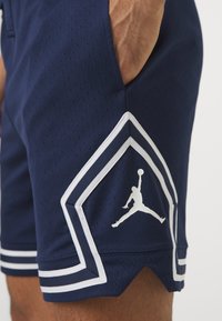 Mornarski atletski šorts s perforirano teksturo, belimi naglasnimi črtami in velikim belim Air Jordan logotipom na spodnjem stranskem panelu.