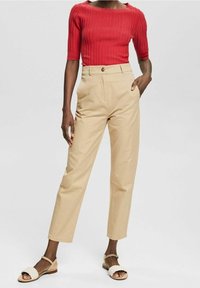 Top rosso a costine con maniche corte, pantaloni beige a vita alta e sandali in tessuto bianco. Texture in tessuto naturale, vestibilità rilassata.