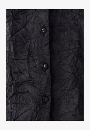 Juodas marškinėliai su mygtukais, pagaminti iš susiraukšlėjusios medžiagos, turintys keturis juodus mygtukus ir tekstūruotą paviršių su matomomis raukšlėmis ir įlenkimais.