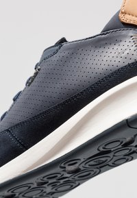 Sneakers blu scuro con parte superiore in pelle perforata e accenti in suede. Presentano una suola intermedia bianca e una suola esterna in gomma nera con motivo circolare.