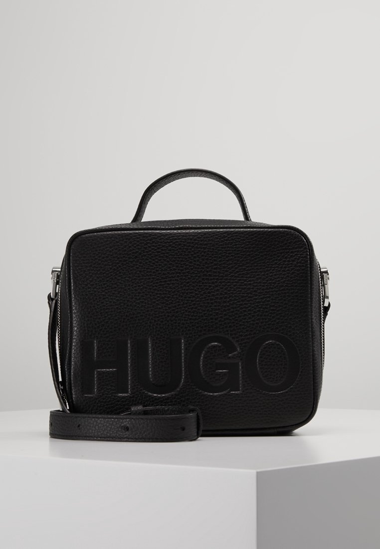 Schwarze Lederhandtasche mit strukturiertem Oberflächen, ausgestattet mit einem Griff oben, einem verstellbaren Schultergurt und dem eingeprägten "HUGO"-Logo auf der Vorderseite.
