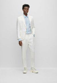 Completo di lino bianco con una camicia color blu chiaro e sneakers beige. Il completo presenta un giacca a un bottone e pantaloni dalla vestibilità comoda.