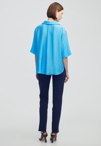 Krátký rukáv, světle modrá blůza z hladkého materiálu s límečkem. V kombinaci s tmavomodrými kalhotami a černými sandály na vysokém podpatku.