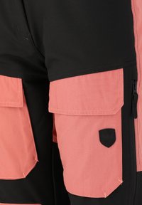 Zwarte shorts met lichtroze accenten, voorzien van cargozakken, ritsen en een zwart logo patch. De stof lijkt duurzaam en gestructureerd.