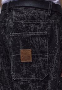 Μαύρα τζιν σορτς με υφή σε αφηρημένο μοτίβο, με καφέ δερμάτινη ετικέτα στην πίσω τσέπη και λευκές ραφές ως διακοσμητικά στοιχεία.