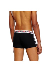 Schwarze Boxer-Shorts aus dehnbarem Material, ausgestattet mit einem weißen Bund und rotem sowie schwarzem Branding. Seitliche Streifen verleihen ein Gestaltungselement.