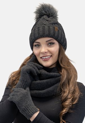 Berretto lavorato a maglia nero con pompon in pelliccia, guanti abbinati e una sciarpa textured. I materiali sembrano caldi ed elasticizzati, adatti per essere indossati in inverno.