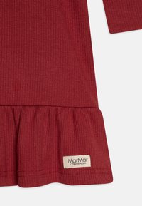 Rød ribbet kjole med utsvingt hemline og en off-white etikett med "MarMar COPENHAGEN" nederst. Myk strikket stoff.