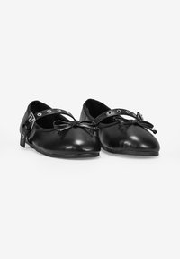 Chaussures en cuir noir avec un petit talon, bout arrondi, détail de lacets et sangle avec des découpes circulaires pour un design supplémentaire. Texture lisse, style minimaliste.
