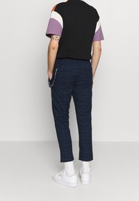 Camisa de manga corta negra y multicolor combinada con pantalones recortados de cuadros en color azul marino. Presenta una cintura elástica y bolsillos laterales.