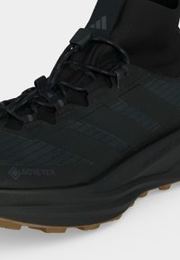 Μαύρο sneaker Gore-Tex της Adidas με μεσαία σόλα Boost, υψηλό κολάρο αστραγάλου και κορδόνια με σχέδιο σε ανοιχτό φόντο.