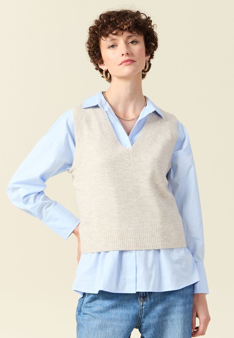 Helles graues gestricktes Vest mit V-Ausschnitt, über einem hellblauen Hemd mit Knöpfen getragen. Verfügt über einen gerippten Saum und eine lässige Passform. Schlichtes und geschichtetes Design.