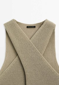Beige knitted sleeveless top featuring a crisscross design at the neckline, with a textured fabric and a label at the center back.