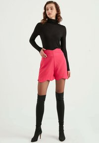 Svart långärmad topp tillsammans med ljusrosa skorts med scallopmönster. Modellen bär svarta knähöga stövlar, vilket visar upp figursydda och släta texturer.