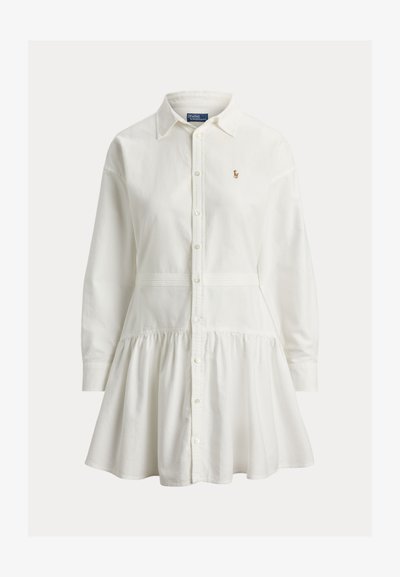 Bela obleka s srajčnim ovratnikom, dolgimi gumbi na sprednji strani, nabranim krilom in majhnim vezenim logotipom na levi strani prsnega koša.