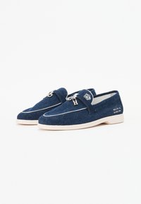 Marineblauwe stoffen loafers met witte stiksels, zilveren hardware en een logo-accent; beige rubberen zool. Ontworpen voor casual gebruik.