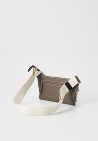 Sac marron texturé avec une sangle réglable crème, doté d'une poche zippée à l'avant et de détails en couture blanche. Design compact et angulaire.
