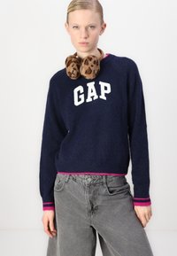 Pulover navy cu litere albe "GAP", dungi roz la guler și manșete, asortat cu blugi lungi gri cu talie înaltă și căști cu imprimeu de leopard.