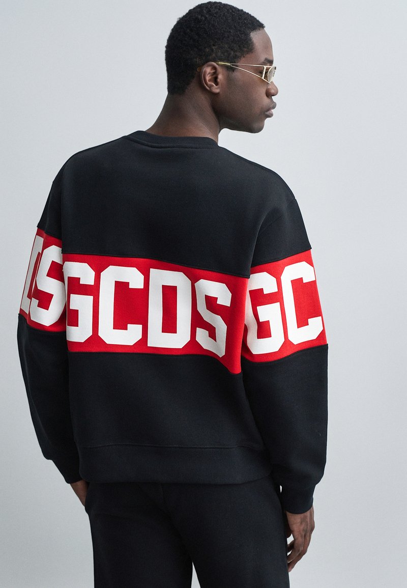 Μαύρη μπλούζα με κόκκινη λωρίδα που φέρει μεγάλες λευκές γράμματα "GC" και "DS", κατασκευασμένη από μαλακό υλικό, με ριμπ μανσέτες και σχέδιο λαιμού τύπου crew.
