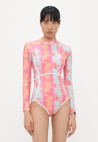 Maillot de bain à manches longues rose avec des motifs floraux turquoise et orange. Accents blancs le long des coutures. Tissu lisse et extensible.