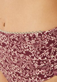 Burgundy mönstrad bikini med blommönster, mjukt tyg, rynkade sidor och en dekorativ silverrand längs midjan.