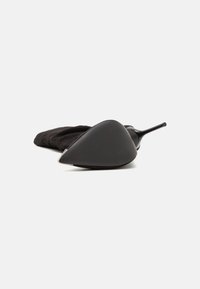 Zapato de tacón alto negro con punta afilada, que presenta un acabado mate texturizado y un elegante acento metálico brillante a lo largo del borde.