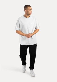 T-shirt grigio oversize con colletto rotondo, abbinato a pantaloni della tuta neri e sneakers bianche, caratterizzato da un design semplice e minimalista.